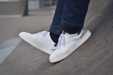 Erkek bacakları, yeni beyaz spor ayakkabılarla, açık hava oyun parkında kapanıyor. Seçici odak