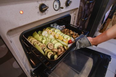 Kadın elleri ızgara için taze sebzelerle tepsiyi fırına koyuyor. Seçici odaklanma. Düşük Dof.