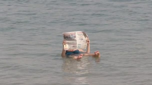 Une femme lit un journal flottant dans la mer morte — Video