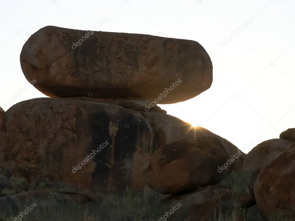 the suns rays appear over a unusual rock at the devils marbles in australia