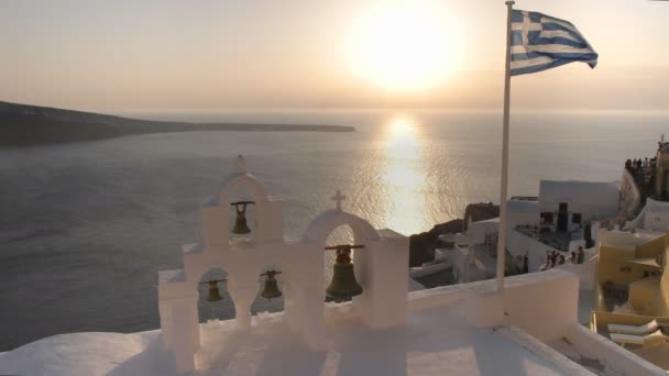 greek flag and four bells at sunset in oia, santorini