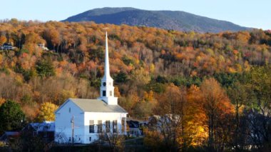 Vermont 'ta beyaz bir kilisenin yakın görüntüsü ve sonbahar yapraklı bir tepe.