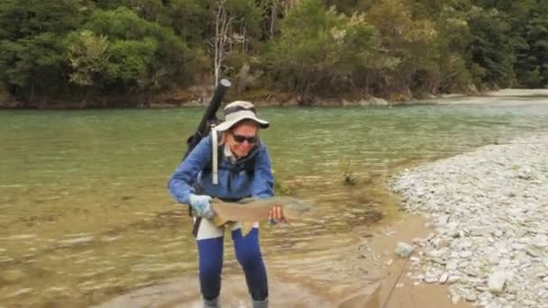 Dişi balıkçı, Yeni Zelanda 'da bir nehirde büyük kahverengi bir alabalık tutuyor. — Stok video