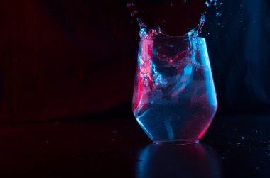 Mavi ve kırmızı renklerle işaretlenmiş su, siyah bir arkaplanda cam bir kadehe sıçrıyor.