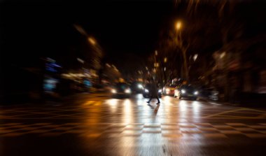 Paris 'te gece vakti caddeden geçen bir adamın bulanık görüntüsü. Trafik ışıklarında arabalar bekliyor..