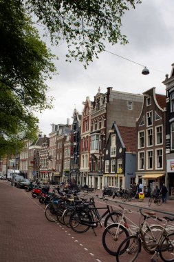 Amstel caddesinde yürüyen insanların görüntüsü, Amsterdam 'da birçok bisiklet parketmiş, tarihi ve geleneksel binalar. Bulutlu bir yaz günü..