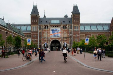 Rijksmuseum 'un önünde yürüyen ve bisiklete binen insanların görüntüsü. Amsterdam 'ın güneyindeki müze meydanında sanat ve tarihe adanmış bir Hollanda müzesidir..