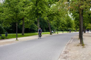 Amsterdam 'daki Vondelpark' ta bisiklet süren, yürüyen, ağaç ve yol gezen insanların görüntüsü. 47 hektarlık bir halk parkı. Bu bir yaz günü..