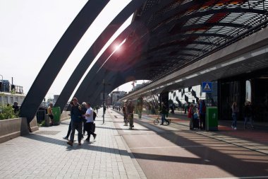 Amsterdam Centraal adlı ana tren istasyonunun arkasında yürüyen ve bisiklete binen insanların görüntüsü. Mercek patlaması etkileri meydana gelir. Güneşli bir yaz günü..