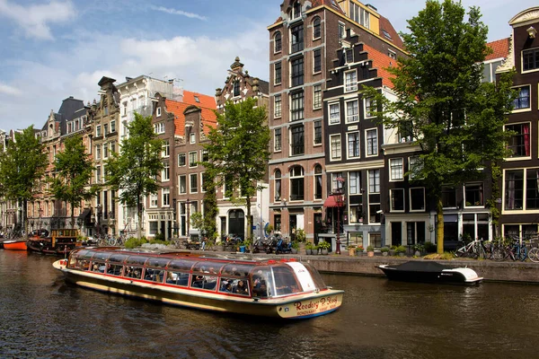 アムステルダムのオランダの建築様式を示す大きなクルーズ運河ツアーボート 駐車自転車 歴史的 伝統的な建物の眺め 晴れた夏の日です — ストック写真