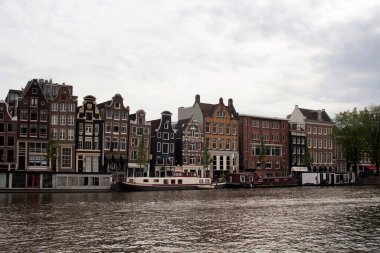 Amstel Nehri manzarası, kanal evleri ve Amsterdam 'daki Hollanda mimari tarzını yansıtan tarihi, geleneksel ve tipik binalar. Bulutlu bir yaz günü..