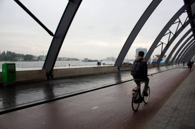 Amsterdam Centraal adlı ana tren istasyonunun arkasında bisiklet süren bir adamın bulanık görüntüsü. Yağmurlu bir yaz günü..