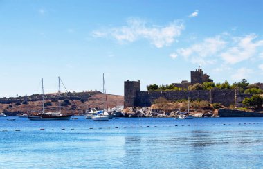 Bodrum kalesinin önündeki turkuaz suya park edilmiş lüks yatlar (yelkenli tekneler). Görüntü Ege ve Akdeniz kıyı yaşam tarzının kültürünü gösteriyor.