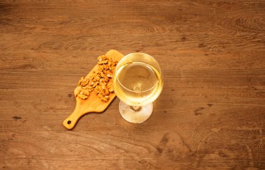 Tahta masada bir bardak beyaz şarap ve ceviz.