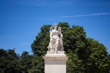 Paris Jardin Des Tuileries 'deki kanatlı kadın heykeli. Arka planda ağaçlar ve mavi gökyüzü var.
