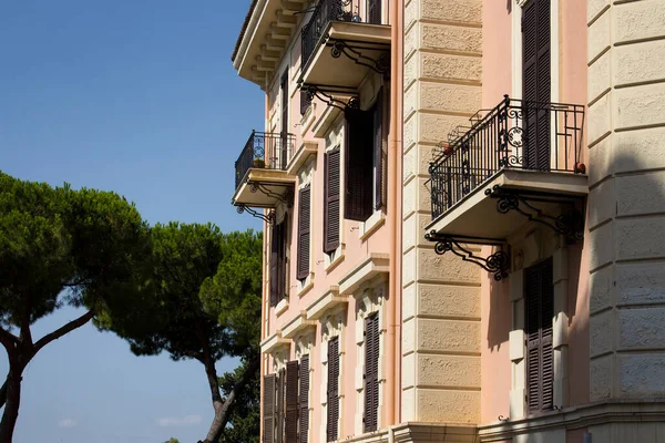 Side view of a traditional residential building showing Italian architecture in Rome. Mediterranean pine trees and blue sky background are in the view.