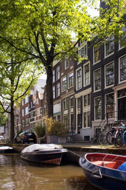 Kanal manzarası, ağaçlar, park edilmiş bisiklet ve tekneler, Amsterdam 'da Hollanda mimari tarzını gösteren tarihi ve geleneksel binalar. Güneşli bir yaz günü..
