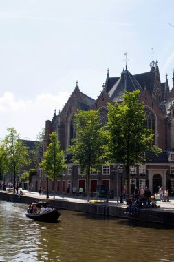 Kanalda küçük bir tekneye binip 13. yüzyıl Amsterdam 'daki The Oude Church' ün önünde tur yapan insanların görüntüsü. Birçok insan sokaklarda takılır. Güneşli bir yaz günü..