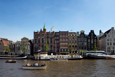 Amstel Nehri 'nde tekne turu yapan insanların görüntüsü. Arka planda tarihi, geleneksel ve tipik binalar var. Açık mavi gökyüzü güneşli bir yaz günüdür..