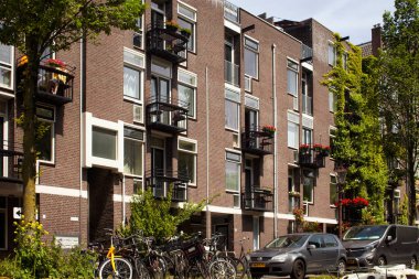 Amsterdam 'daki tipik binalar, ağaçlar, park edilmiş arabalar ve bisikletlerin manzarası. Güneşli bir yaz günü..