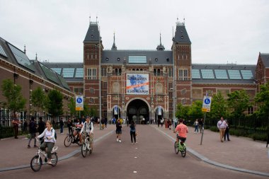 Rijksmuseum 'un önünde yürüyen ve bisiklete binen insanların görüntüsü. Amsterdam 'ın güneyindeki müze meydanında sanat ve tarihe adanmış bir Hollanda müzesidir..