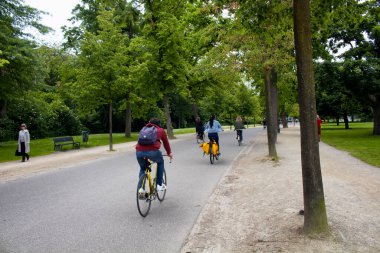 Amsterdam 'daki Vondelpark' ta bisiklet süren, yürüyen, ağaç ve yol gezen insanların görüntüsü. 47 hektarlık bir halk parkı. Bu bir yaz günü..
