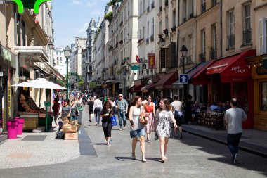 Paris 'te güneşli bir günde Montorgueil Caddesi' nde insanlar yürür. Manzarada kafeler, küçük dükkanlar ve Fransız mimari tarzı binalar yer alıyor