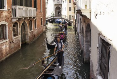 Turistler Venedik / İtalya 'daki eski tarihi binalar arasındaki kanallarda gondollara biniyorlar..