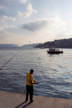 İstanbul 'un Istinye bölgesinde boğazdan balık yakalamaya çalışan bir adam. Arka planda küçük balıkçı teknesi ve FSM köprüsü var..