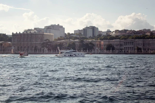 İstanbul Boğazı 'ndaki tarihi binanın önünden geçen beyaz bir yatın görüntüsü. Avrupa tarafındaki binalar da manzarada.