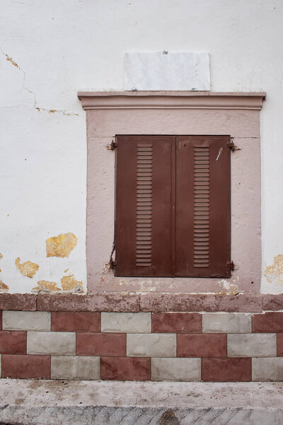 Close up view of closed shutters and stone wall of historical house in Cunda (Alibey) island. Street sign is placed above window.