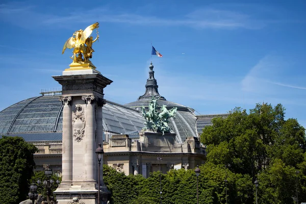 ポンアレキサンドル3世橋のグランドパレと黄金の像の眺め 建物の上にフランスの旗の波 背景には木々や青空が広がっています — ストック写真