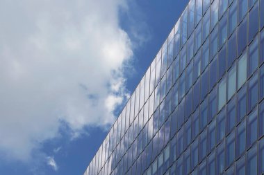 Modern, cam binanın alt manzarası. Bulutlar ve cam yüzeyindeki yansımaları dramatik bir atmosfer yaratır..