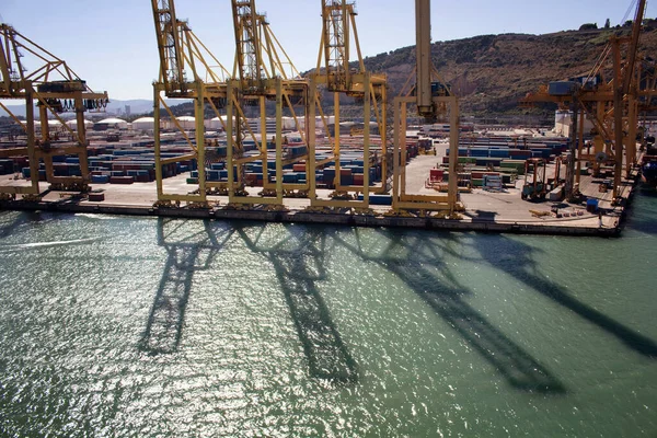 Aerial view of shadows of big, giant cranes on sea surface at Barcelona port. Many containers are in the background.