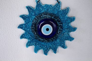 Decorative, blue wall object in shape of sun and made with evil eye. It is on white plaster background. clipart