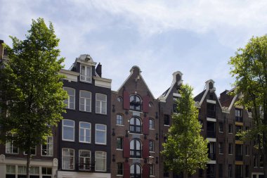 Amsterdam 'da Hollanda mimari tarzını ve ağaçlarını gösteren tarihi, geleneksel ve tipik binaların manzarası. Mavi gökyüzü güneşli bir yaz günü..
