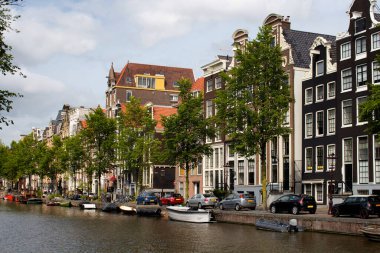 Kanal manzarası, park edilmiş tekneler, arabalar, ağaçlar ve Amsterdam 'da Hollanda mimari tarzını gösteren geleneksel binalar. Bu bir yaz günü..