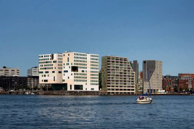 Arka planda modern konut binaları olan yelkenli ve kanal manzarası. Açık mavi gökyüzü güneşli bir yaz günüdür..