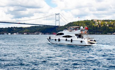 Beyaz lüks yat / tekne İstanbul 'da Avrupalı ve Asyalı taraflar arasında Boğaz' ı geçiyor. Hava bulutlu bir sonbahar günü. Arka planda FSM (Fatih Sultan Mehmet) köprüsü.
