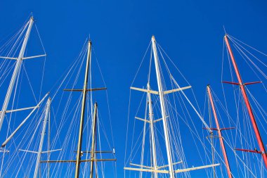 Bodrum limanındaki açık mavi gökyüzü arka planına sahip yat direkleri ve yelkenli teknelerin alt görüntüsü.