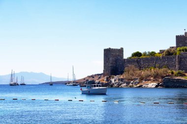 Bodrum kalesinin önündeki turkuaz suya park edilmiş lüks yatlar (yelkenli tekneler). Görüntü Ege ve Akdeniz kıyı yaşam tarzının kültürünü gösteriyor.