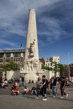 Amsterdam 'daki Ulusal Anıt' ın önünde takılan insanların görüntüsü. Mavi gökyüzü güneşli bir yaz günü..