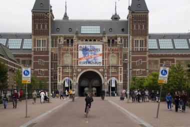 Rijksmuseum 'un önünde yürüyen ve bisiklete binen insanların görüntüsü. Amsterdam 'ın güneyindeki müze meydanında sanat ve tarihe adanmış bir Hollanda müzesidir..