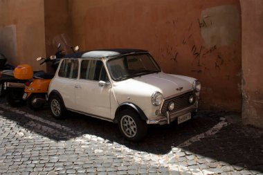 Retro, beyaz, küçük, eski bir araba Roma 'da Trastevere caddelerinden birinde motosikletin yanına park edilmiş.