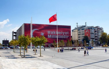 Taksim Meydanı manzarası. Dev bir direkte büyük bir Türk bayrağı dalgalanıyor. Darbe girişiminden sonra Atatürk Kültür Merkezi 'ne siyasi mesaj asıldı. İnsanlar etrafta dolanıyor..