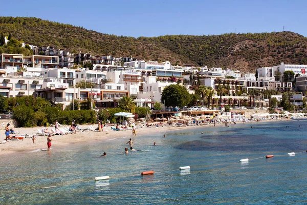 İnsanlar Bodrum şehir merkezinin yakınındaki Icmeler plajında yüzüyor. Güneşli bir yaz günü. Geleneksel, beyaz, tipik yazlık evler bölgenin mimari tarzını yansıtıyor.
