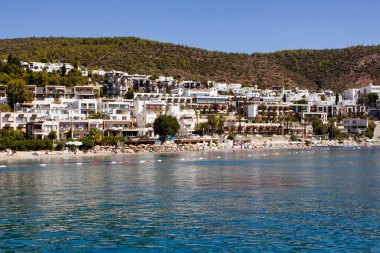 İnsanlar Bodrum şehir merkezinin yakınındaki Icmeler plajında yüzüyor. Güneşli bir yaz günü. Geleneksel, beyaz, tipik yazlık evler bölgenin mimari tarzını yansıtıyor.