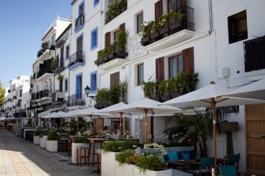 İbiza 'daki geleneksel, beyaz, tipik binaların manzarası. Görüntü adanın mimari tarzını yansıtıyor. Olay yerinde demir parmaklıklar, kafeler, restoranlar ve balkonlardaki pek çok bitki bulunuyor..