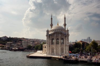 İstanbul 'un bulutlu gökyüzü arka planına sahip Boğaz' daki tarihi ve ünlü Ortakoy Camii 'nin (Ortakoy Camii) manzarası. Turistler, yerel halk ve Beşiktaş bölgesindeki binalar manzarada.