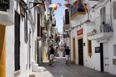 Gündüz vakti İbiza 'nın gay caddesinde üç genç adam yürüyor. Dar sokak ve beyaz, geleneksel binalar adanın yaşam tarzını ve kültürünü yansıtıyor. Calle de la Virgen caddesi..